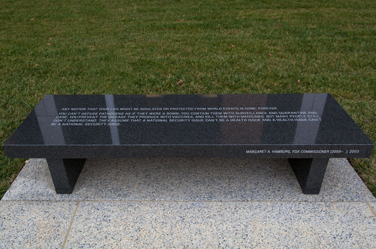 Inscribed granite bench stating 'Any notion that your life might be insulated or protected from world events is gone, forever. You can't defuse pathogens as if they were a bomb; you contain them with surveillance and quarantine and care; you prevent the disease they produce with vaccines, and kill them with medicines, but many people still don't understand. They assume that a national security issue can't be a health issue and a health issue can't be a national security issue'.