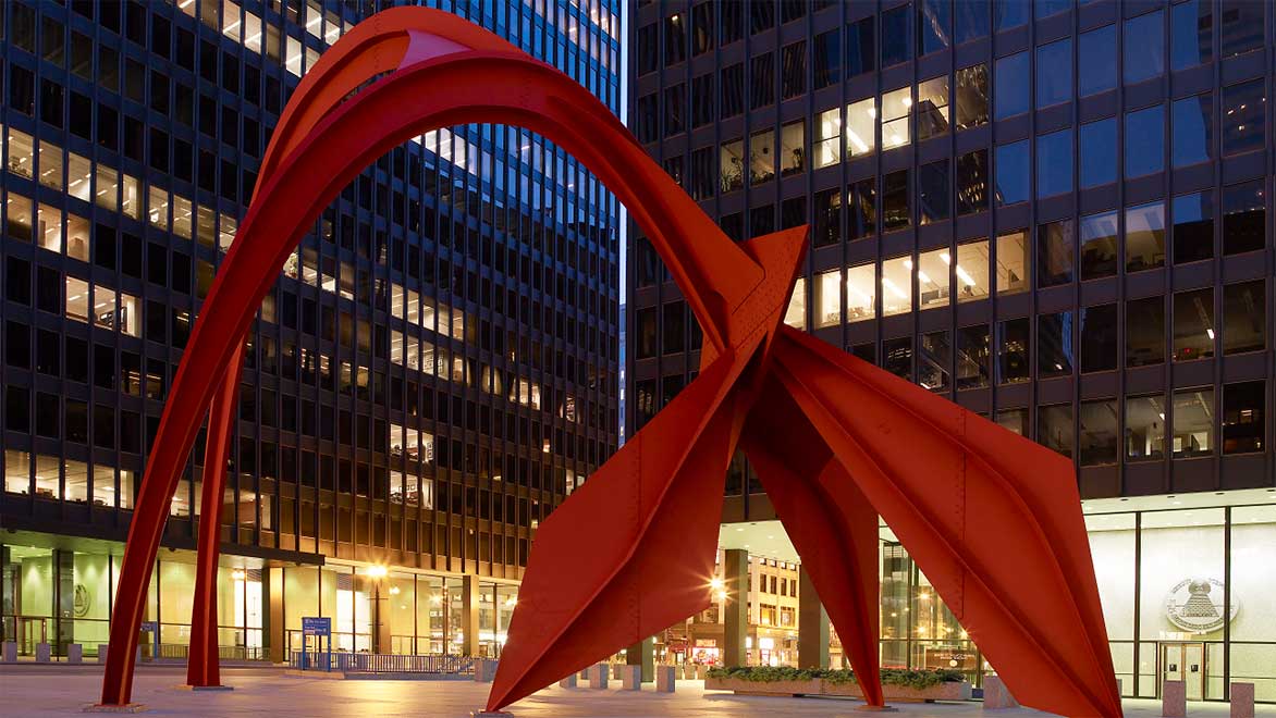 Exterior night shot of red-orange Calder Flamingo sculpture with Kluczynski Federal Building behind on right and Dirksen U.S. Courthouse on left