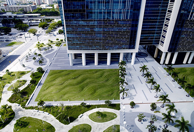 Sculpted lawns that mimic rippling water or sand with a path leading through it and trees and a building in the background