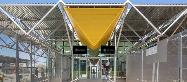 Entrance to geometric metal and glass building with yellow canopy and blue sky