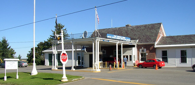 Three-part white and red brick building with a cover over two drive-through lanes, a stop sign and flags