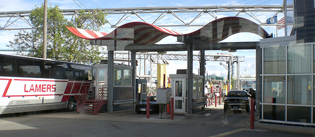 Red and white wavy cover over two drive-through lanes and booths, next to a windowed building with a tour bus on the left