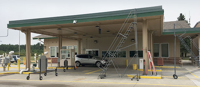 One-story tan building with green trim and a canopy that extends over three driving lanes, with two rolling ladders, a rolling stop sign, and a silver vehicle in the lane closest to the building entrance