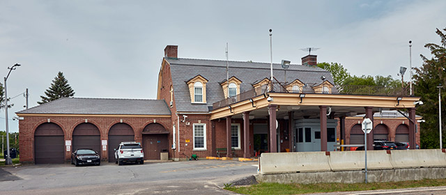 A barn-style red building with a canopy and three lanes below it, with four arched brown garage bays and two vehicles to the left and trees in the background