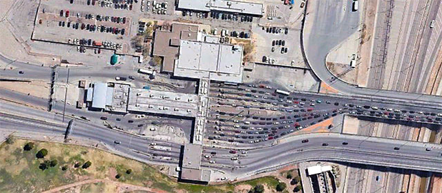 Sky view of a cluster of buildings, one with a canopy over several separated lanes, with cars, parking lots, and grassy area