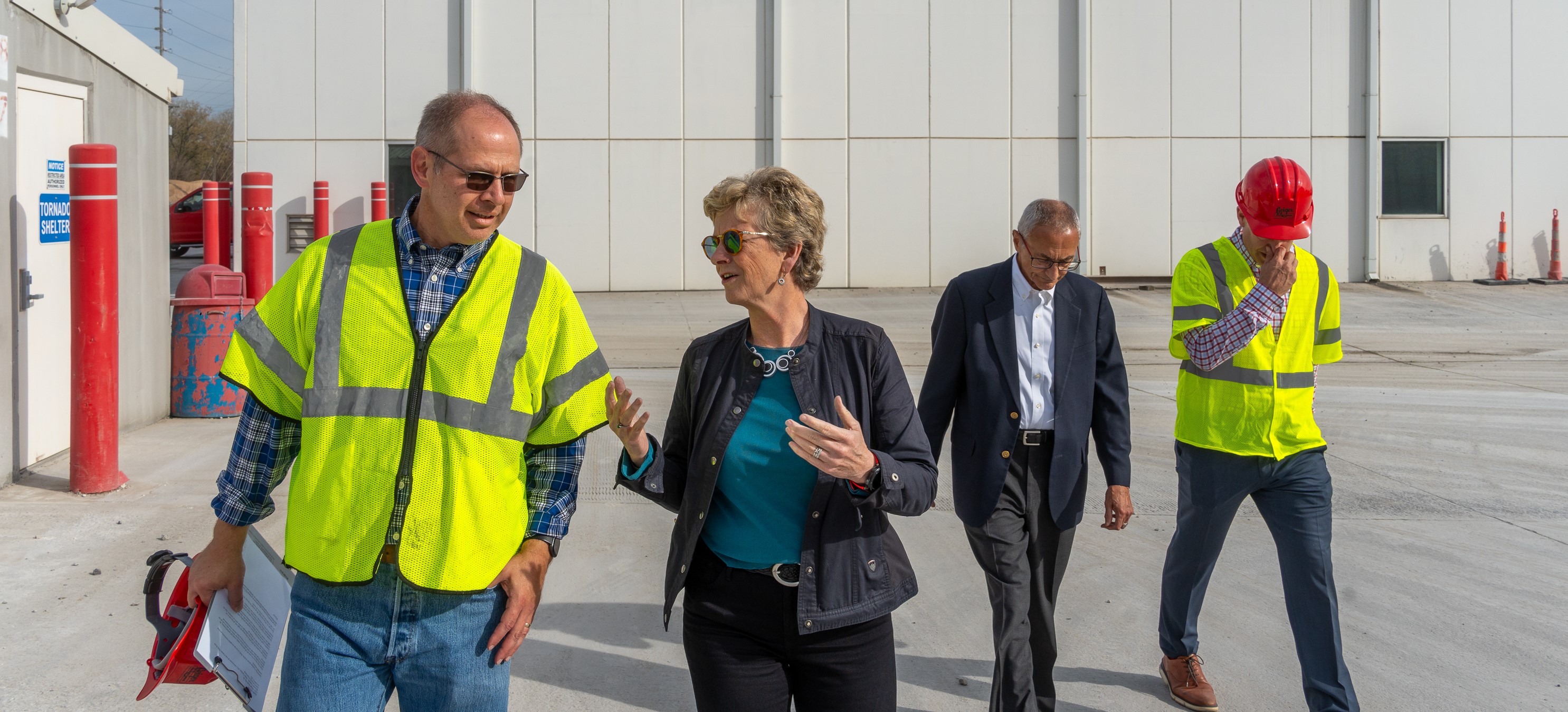 Administrator Robin Carnahan wearing a bright yellow construction vest walking with three men also wearing yellow construction vests