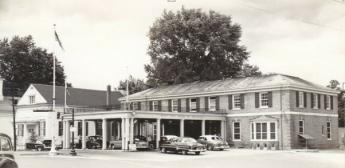 a building with a car port and cars underneath and a flag pole in front