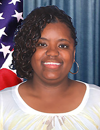 Lisa Cason, a woman smiling, wearing a white shirt, standing in front of a curtain background with an American flag over right shoulder.
