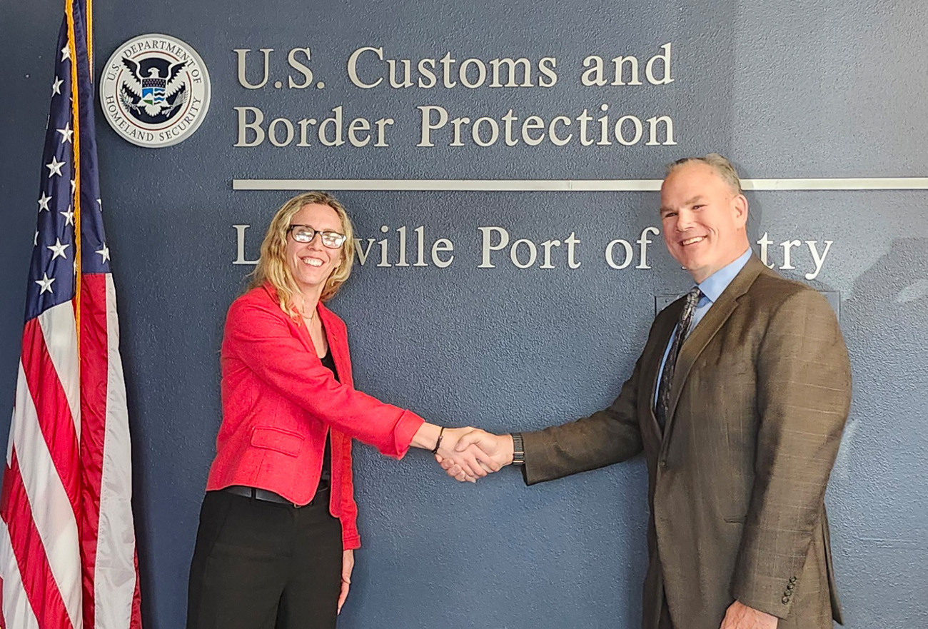 Diana Schlumpf, GSA San Diego Service Center Director, is shaking hands with a member of CBP.  The American Flag hangs just behind Diana.