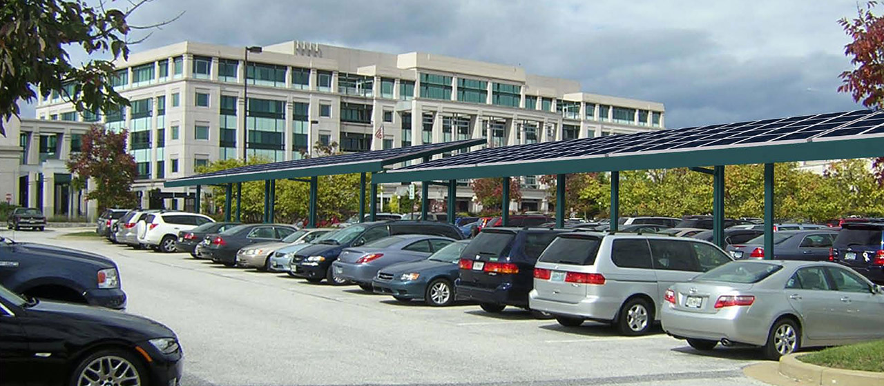Angle view of white stone multi-level building with parking lot in front, with cars and solar panels