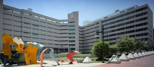 Multi-level beige building with courtyard in front with colorful sculptures and some trees