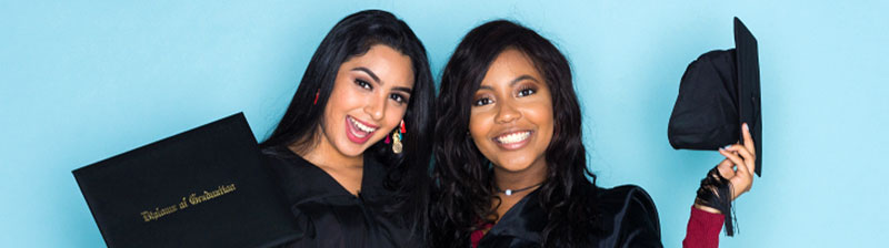 Two smiling people of color in graduation attire in front of a blue background