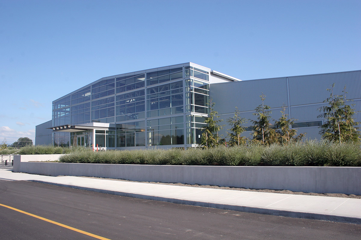 Daytime exterior of a glass and metal low building next to road with blue sky