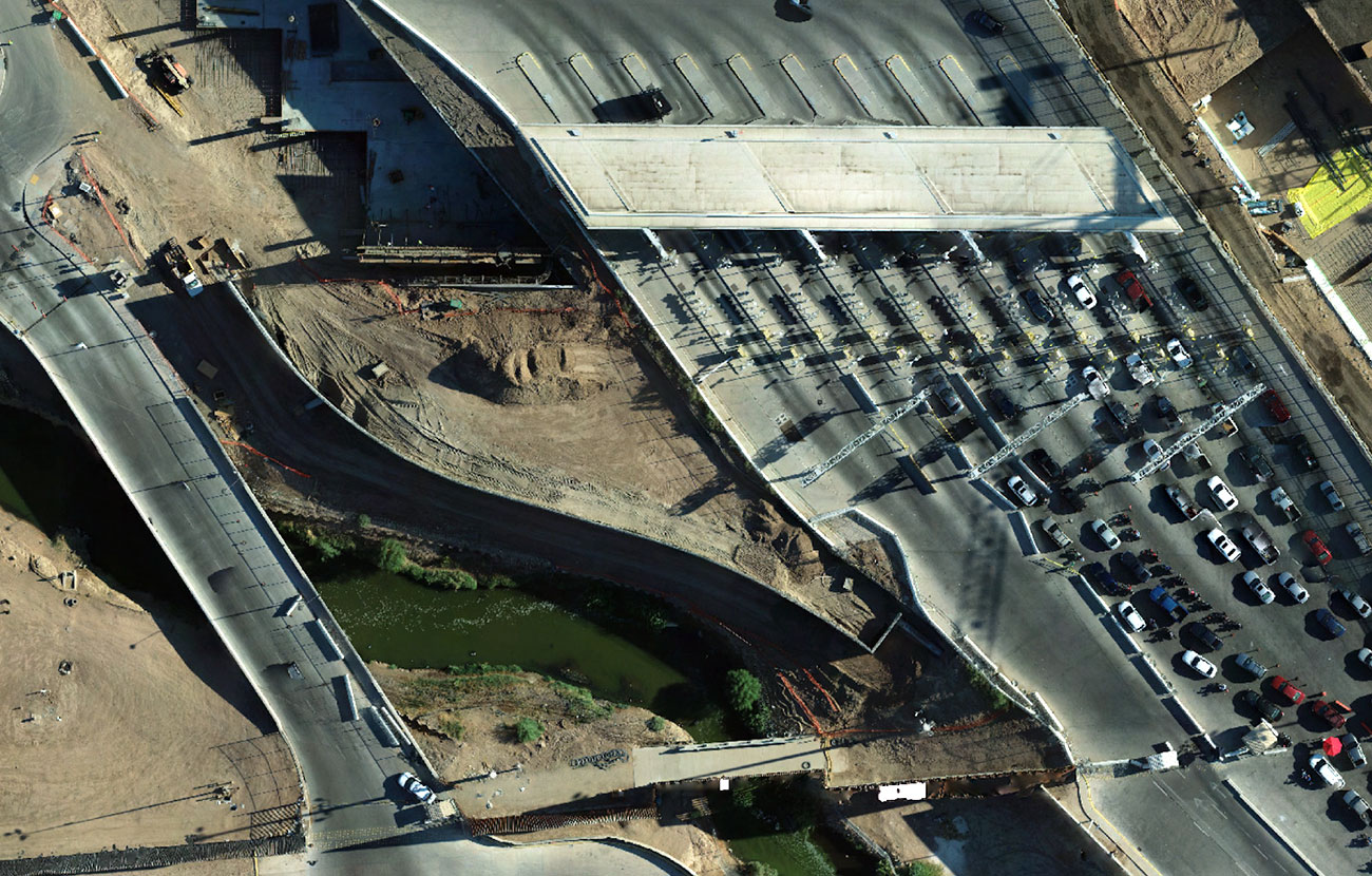 Overhead view of several lanes of vehicles lined up to go under a large canopy, next to a large area of construction