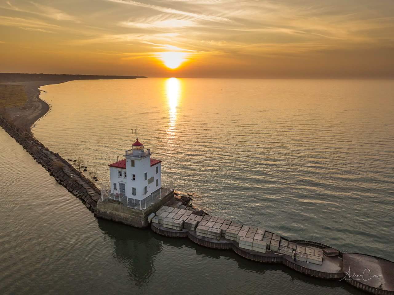 A white lighthouse with a red roof on the water at sunset