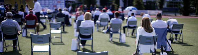 Socially distant chairs at an outdoor event on a lawn facing a screen in the background
