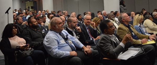 crowd shot of several dozen people watching a presentation at NCR