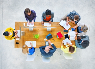 Group of 10 people sitting around a table working together