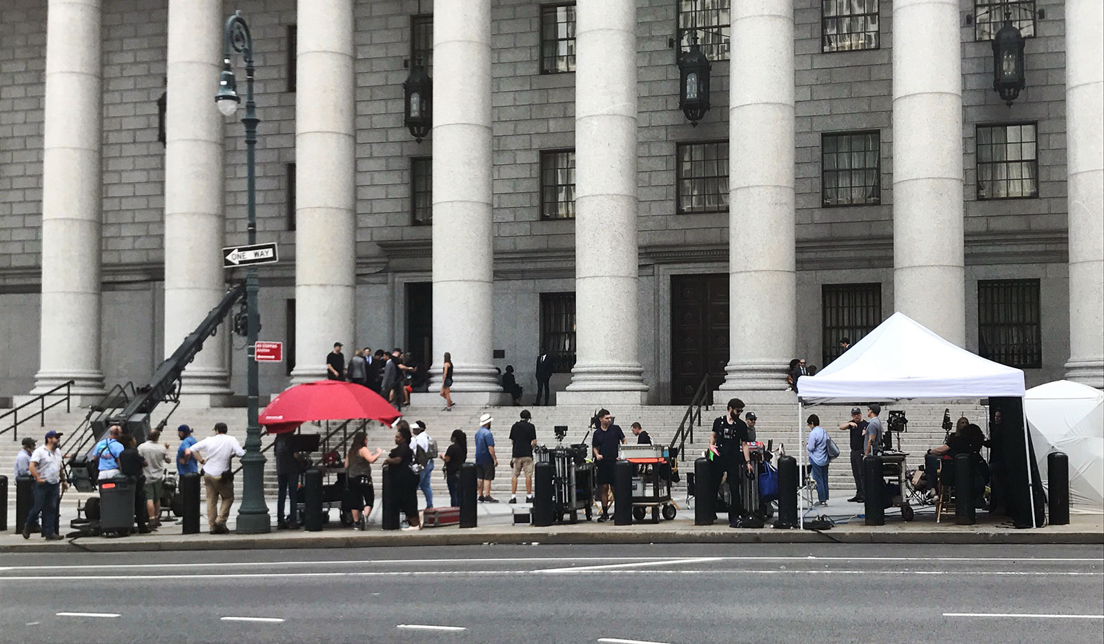 A film crew and equipment on the sidewalk outside of a gray governmental-looking building with big columns