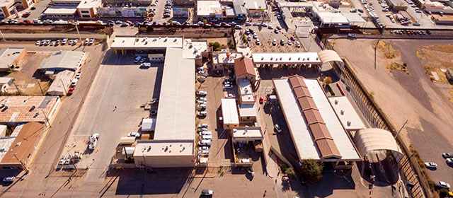 Aerial view of a grouping of low buildings and surrounding pavement and parking lots and parked cars