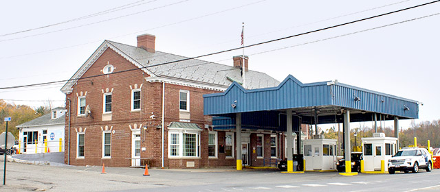 Two level brick building with two chimneys and a blue driveway cover with two booths and yellow ground posts