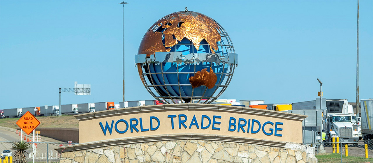Large globe sculpture above sign on a stone wall catwith text World Trade Bridge