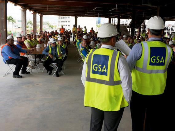 Darren Gomez (right), GSA Northeast and Caribbean acting regional commissioner for Public Buildings Service, delivers remarks with Spanish interpretation help from Edgar Hernandez, GSA Caribbean Field Office manager, at the San Juan FBI complex topping-out ceremony May 30 in Hato Rey, Puerto Rico. Ceremony attendees included FBI dignitaries from Washington, D.C. and the local area, GSA Region 2 employees, and general contractor Walsh Group dignitaries, local workers and subcontractor staff. (Photo by Mike H