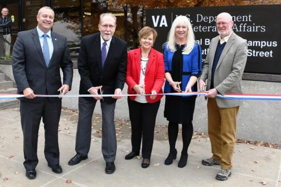 Five people stand behind a ribbon, each holding a pair of scissors, and a U.S. Department of Veterans Affairs sign behind them.