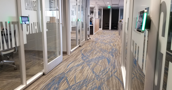 2300 Main hallway showing small glass enclosed conference and huddle rooms with digital display devices lower to the ground.
