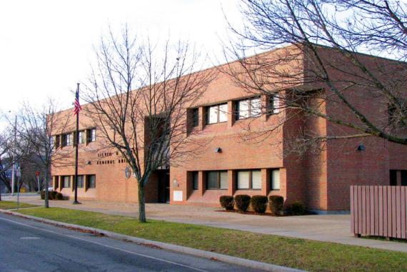 a brown building with trees and an american flag in front