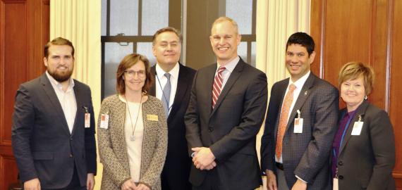 Six people pose for a photo in a conference room