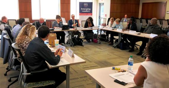 Sixteen people sitting in a rectangle-shape of tables with a banner in the back that says &quot;SBA Emerging Leaders&quot;