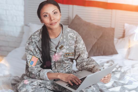 A woman in a military uniform sits on a bed