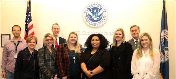 Three men and six women stand in front of a wall with DHS seal, U.S. Citizenship and Immigration Services and U.S. and DHS flags