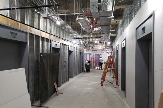 A hallway under construction with elevator doors along both sides, an unfinished ceiling and ladders and other materials
