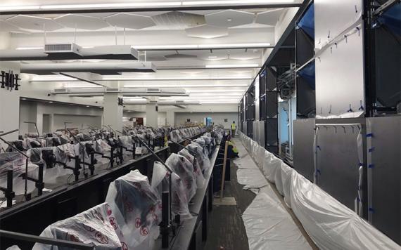 Large room under construction with four rows of workstations facing a large wall of screens