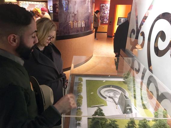 Two people overlook a glass-covered architectural model of a building and circular area