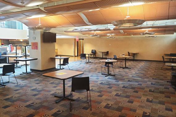 A cafeteria seating area with tables spaced far apart and one chair at each table.