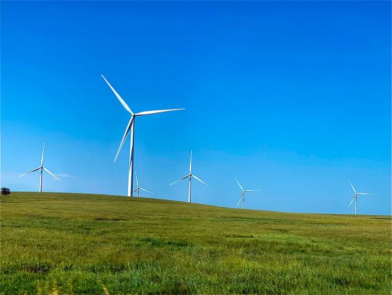 Six white wind turbines in a very green field with a very blue sky