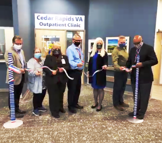 Seven men and women wearing face-coverings hold scissors in front of a sign that reads: Cedar Rapids VA Outpatient Clinic