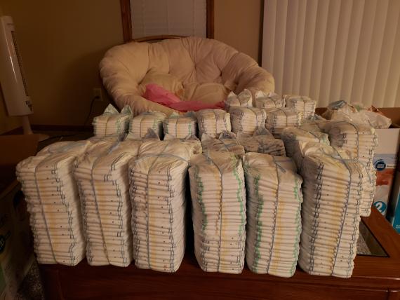 Stacks of disposable baby diapers positioned in front of a cushioned chair.