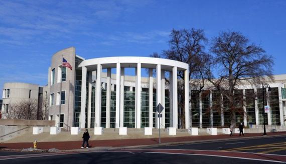 springfield courthouse with columns and an american flag to the left with a woman walking on the sidwalk in front