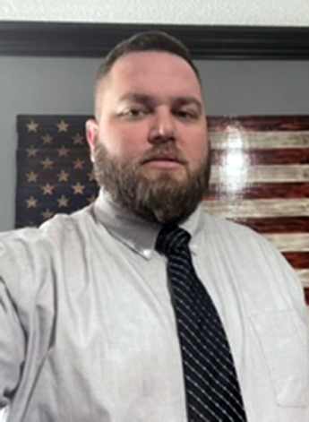Person in business shirt and tie standing in front of an American flag on canvas.
