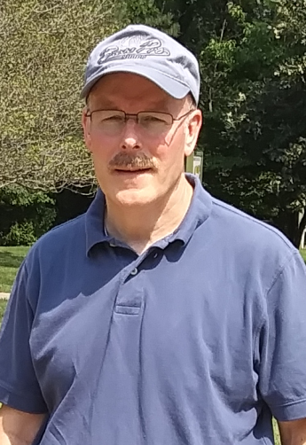 Person in collared polo shirt and hat standing outside.