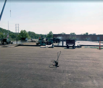 Large flat roof with visible tar, large equipment and a crane in the background