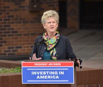 Woman with short blonde hair with scarf and black jacket at podium
