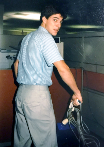 Cy Houston looks over his right shoulder while pushing a vacuum in an office.