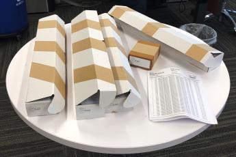 Four long rectangle boxes with a small box and a packet of papers sit on a small white round table