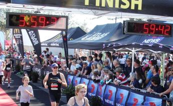  A light-haired young girl and man run outdoors under two marquees that read: 3:59:39 and 59:42.