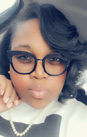 A headshot of Kandice Boykin, a female with shoulder length dark hair with her hand touching her face, wearing glasses, a pearl necklace and a black and white shirt. 